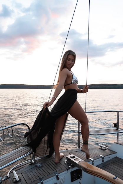 Gorgeous fit woman standing on yacht deck and admiring sea at sunset