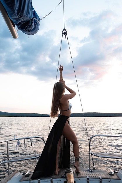 Gorgeous fit woman standing on yacht deck and admiring sea at sunset