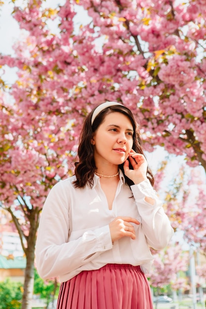 Gorgeous gentle caucasian woman under blooming pink sakura tree copy space