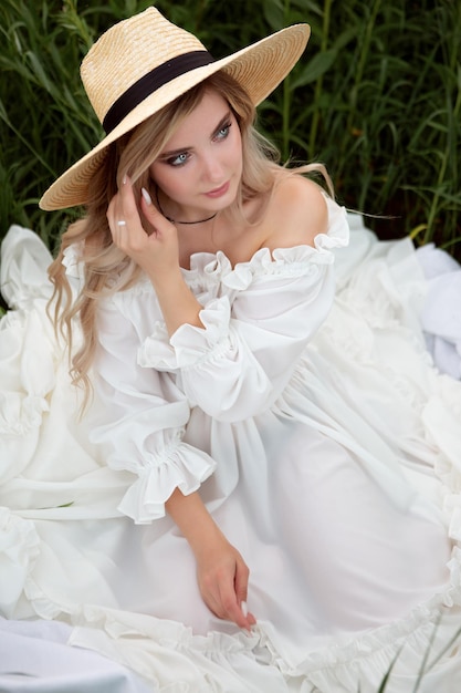 A gorgeous romantic young woman in a white light dress and a straw hat