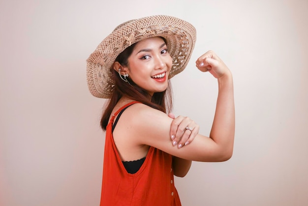 Gorgeous strong young Asian woman with orange dress and straw hat showing biceps and smiling Indonesian girl strong concept