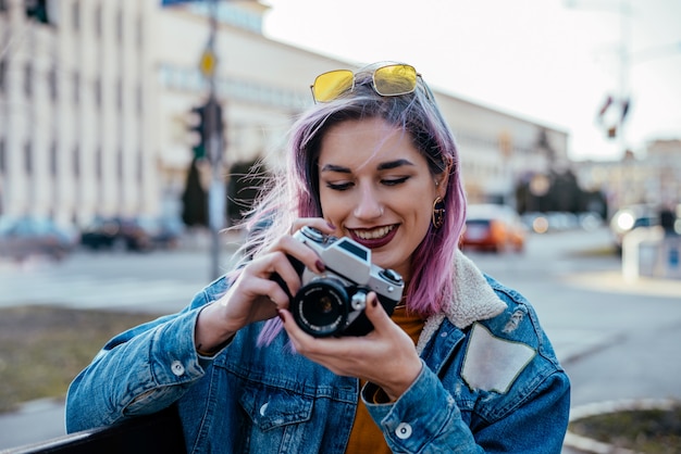 Gorgeous urban girl photographer sitting at city street, using camera.