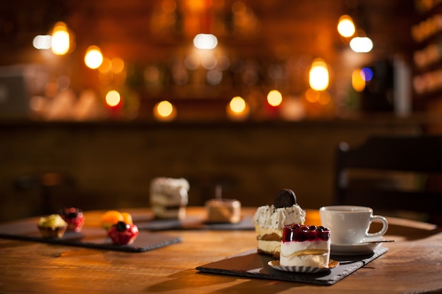 Gorgeous view of different cakes with different flavours over a wooden board in a coffee shop. Delicious variety of cakes in a coffee shop. Tasty cup of coffee.