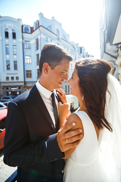 Gorgeous wedding couple walking in city Groom in stylish suit bride in beautiful white dress