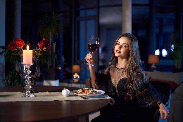 Gorgeous woman in black dress holding glass of red wine