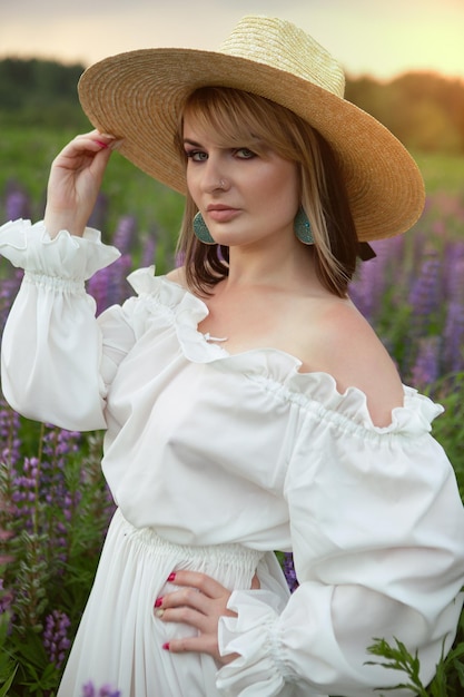 A gorgeous woman in a long light summer dress and hat on a field of flowers