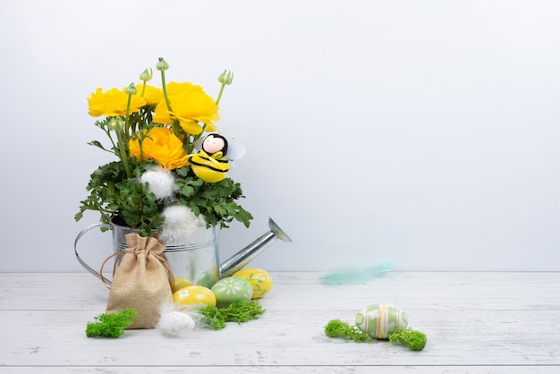 Gorgeous yellow ranunculus buttercups in a metal watering can, bee, Easter eggs with feathers, a canvas bag.