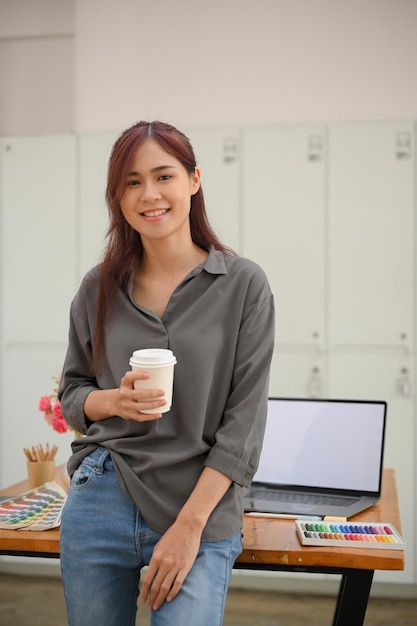 Gorgeous young asian female graphic designer leaning on table and sipping a coffee