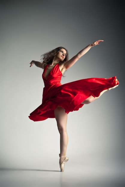 Gorgeous young ballet dancer wearing red dress over dark grey background