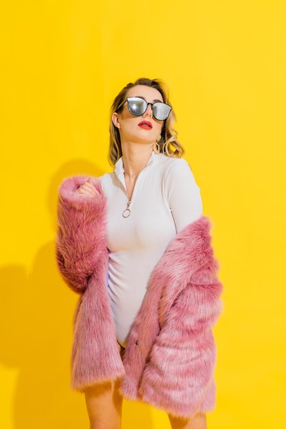 Gorgeous young woman posing in luxurious fur coat and bodysuit Fashion beauty Studio shot