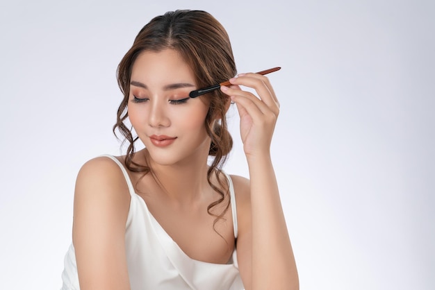 Gorgeous young woman putting black mascara on her long eyelashes with brush