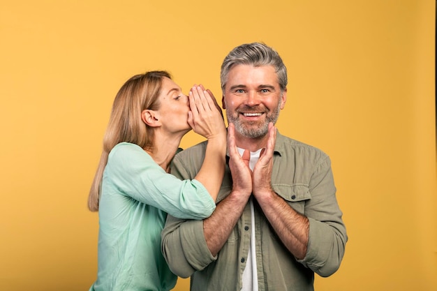 Gossip share advice Woman whispering to her husband on ear happy surprised man listening wife