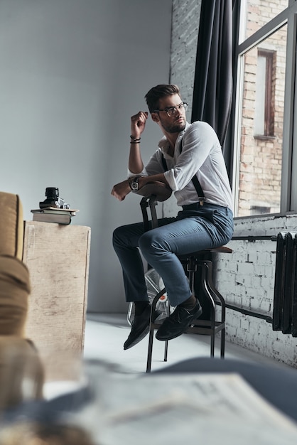 Got something on his mind. Handsome young man looking through the window over his shoulder while sitting on stool