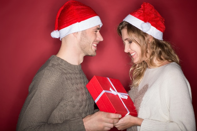 Got something for you. Horizontal portrait of a young handsome man in a Christmas hat giving present to his beautiful happy girlfriend