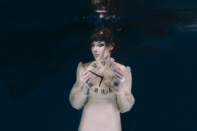 Gothic Spooky woman with clock in her hands in black veil underwater