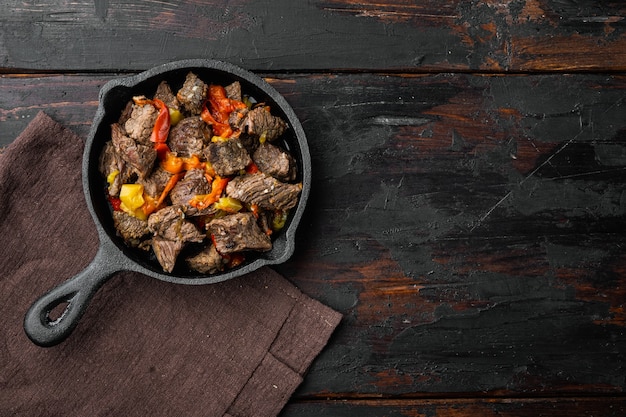 Goulash, beef stew set, in cast iron frying pan, on old dark wooden table, top view flat lay