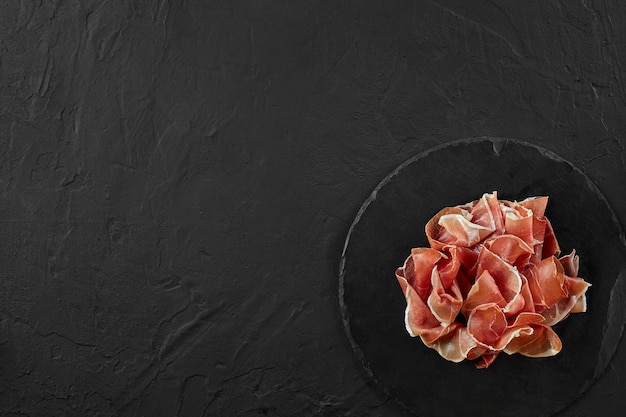 Gourmet manually sliced jamon on black stone slate board against a dark grey background Closeup shot Top view Copy space