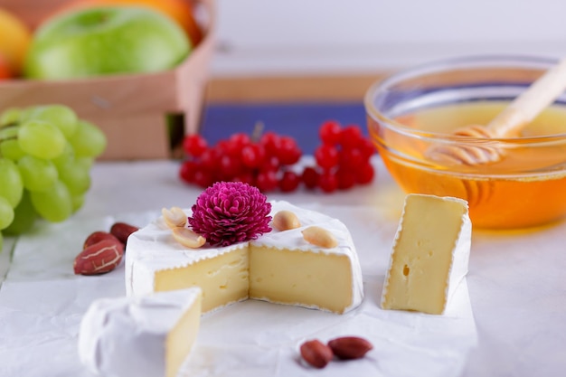 Gourmet white brie or camembert cheese with berries honey and nuts on a white background Still life of cheese honey walnuts and grapes Closeup