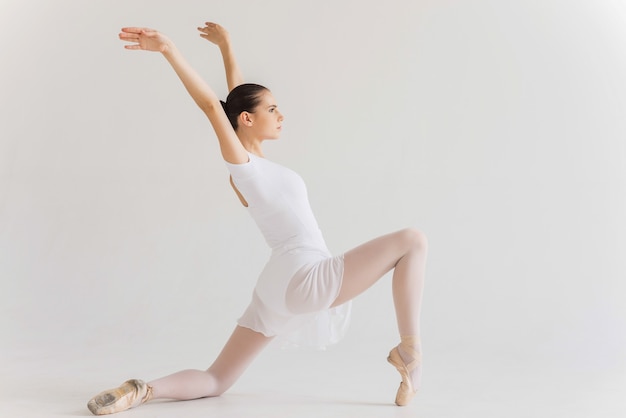 Grace in every move. Side view of beautiful young ballerina in white tutu dancing against white background