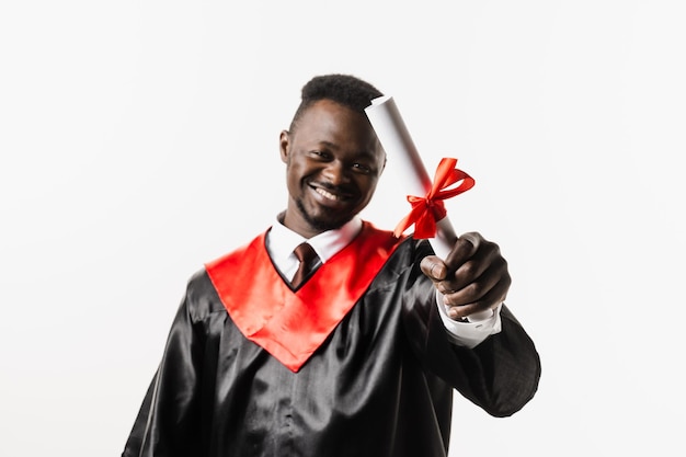 Graduate african man is graduating college and celebrating academic achievement Happy african student in black graduation gown and cap raises masters degree diploma above head on white background