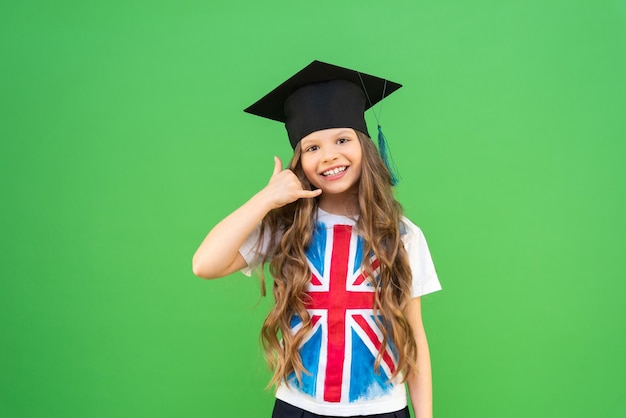 The graduate shows a hand gesture that she is calling on the phone a joyful schoolgirl with curly hair and an English flag painted on a Tshirt