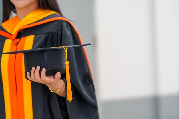 Graduates holding black hats with yellow tassels standing with raised diploma in hand over sunsetConcept education congratulation Graduation Ceremony Congratulated the graduates in University