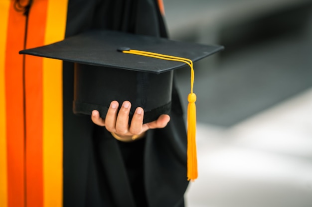 Graduates holding black hats with yellow tassels standing with raised diploma in hand over sunsetConcept education congratulation Graduation Ceremony Congratulated the graduates in University