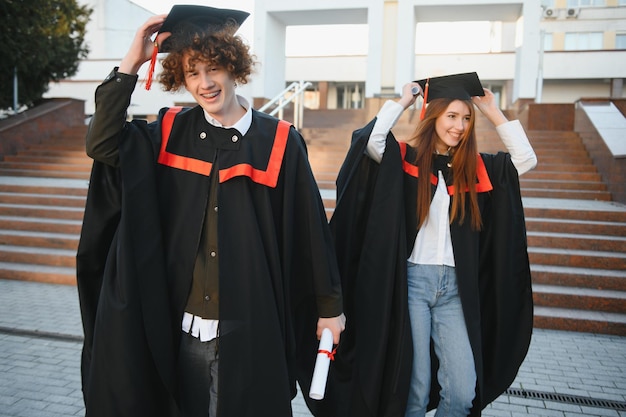 Graduates in mantles with diplomas in hands are standing near university