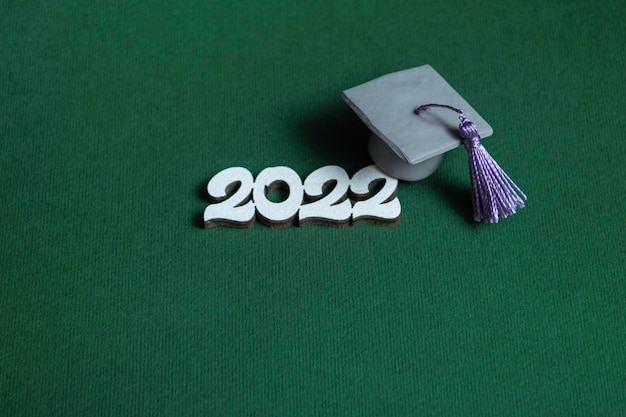 Graduation cap  and numbers 2022 on green background, close up with copy space. Medical education concept.