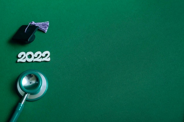 Graduation cap with stethoscope and numbers 2022 on green background close up with copy space Medical education concept