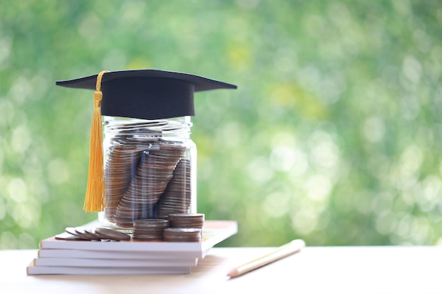 Graduation hat on coins money in the glass bottle on natural green background