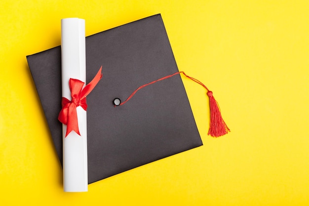 Graduation hat and diploma on yellow background