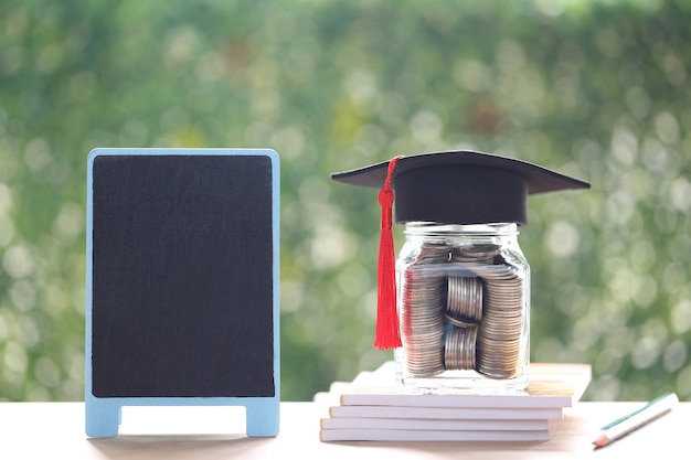 Photo graduation hat on the glass bottle and blackboard on natural green background, saving money for education concept