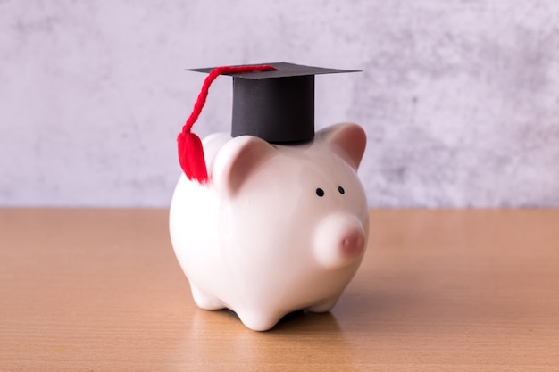 Graduation hat on piggy bank on table, saving money for education concept