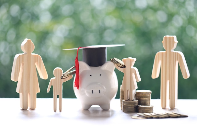 Graduation hat on piggy bank with model family and stack of coins money on natural green background