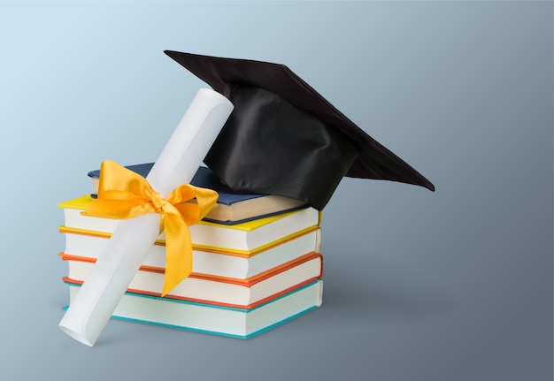 Graduation mortarboard on top of stack of books on  background