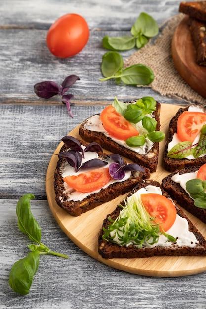 Grain rye bread sandwiches with cream cheese tomatoes and microgreen on gray side view