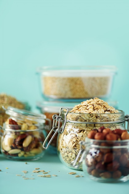 Grains, cereals, nut, dry fruits in glass jars over blue background with copy space. 