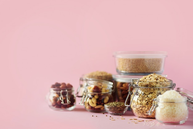 Grains, cereals, nut, dry fruits in glass jars over pink background with copy space. 