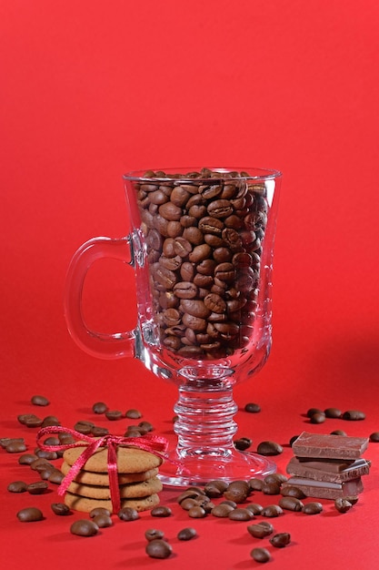 Grains of coffee in a transparent glass cup for drinks with cookies and chocolate on a red backgroun