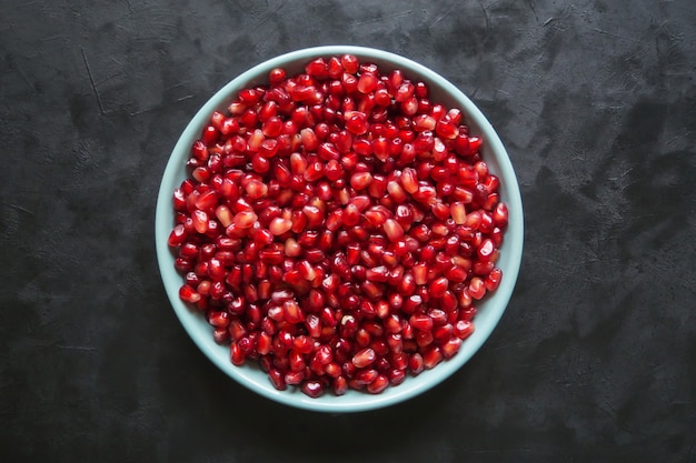 Grains of red pomegranate in a plate on a black table.