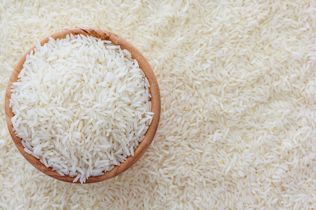 Grains of Thai jasmine rice in wooden bowl on white rice background