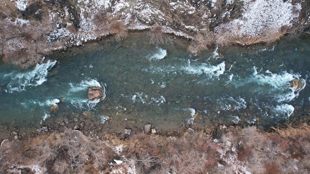 The Grand Canyon in the steppe with the emerald river. A crack in the ground with black stones