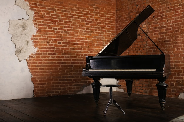 Grand piano with raised lid and stool near brick wall