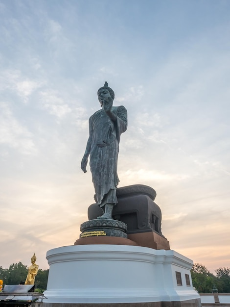 Grand Walking Buddha statue the main statue of Buddhist diocese under twilight sky in Thailand