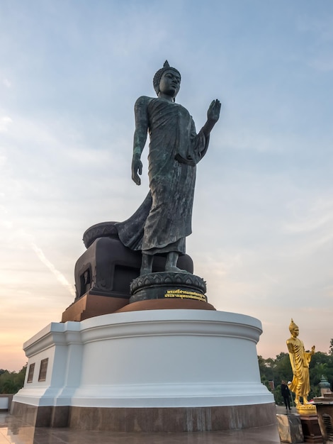 Grand Walking Buddha statue the main statue of Buddhist diocese under twilight sky in Thailand