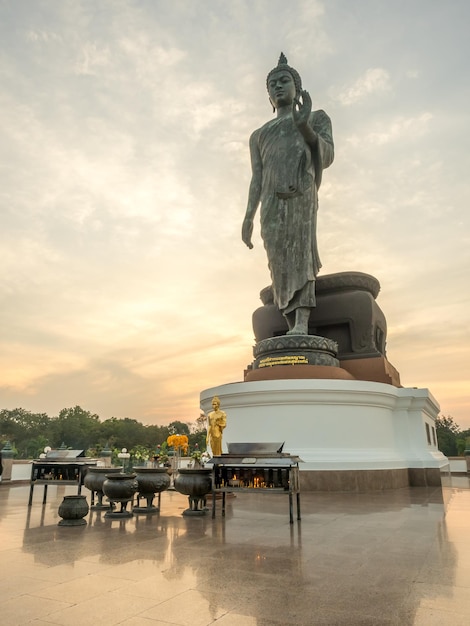 Grand Walking Buddha statue the main statue of Buddhist diocese under twilight sky in Thailand