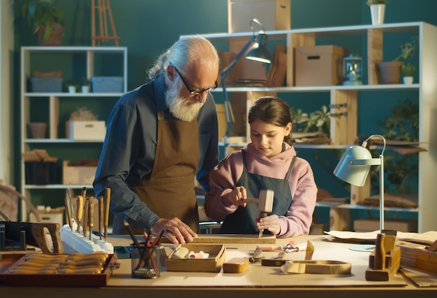 Grandfather carpenter with his teenage granddaughter works in the workshop