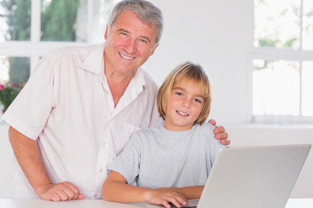 Grandfather and child looking at the camera with smile in front of laptop