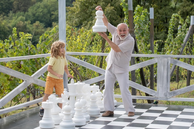 Grandfather and grandson playing chess on big chess board elderly old relative wit child